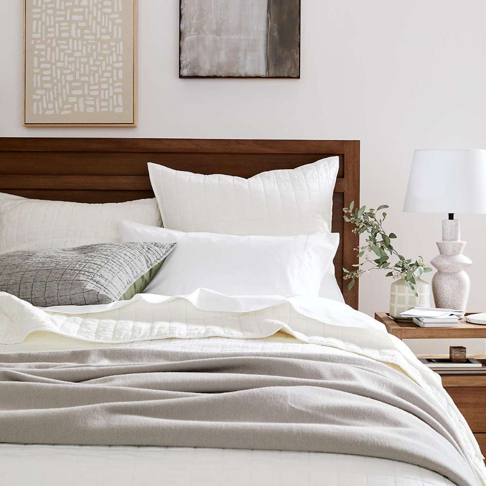 Close-up of Crate & Barrel Keane Solid Driftwood Queen Bed with layered pillows, textured bedding, and a matching wood nightstand