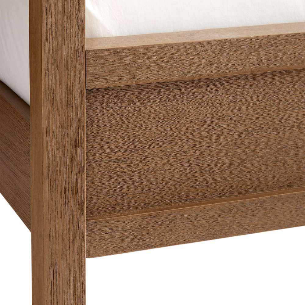 Close-up of the wood frame and footboard corner on Crate & Barrel Keane Solid Driftwood Queen Canopy Bed showing the driftwood finish