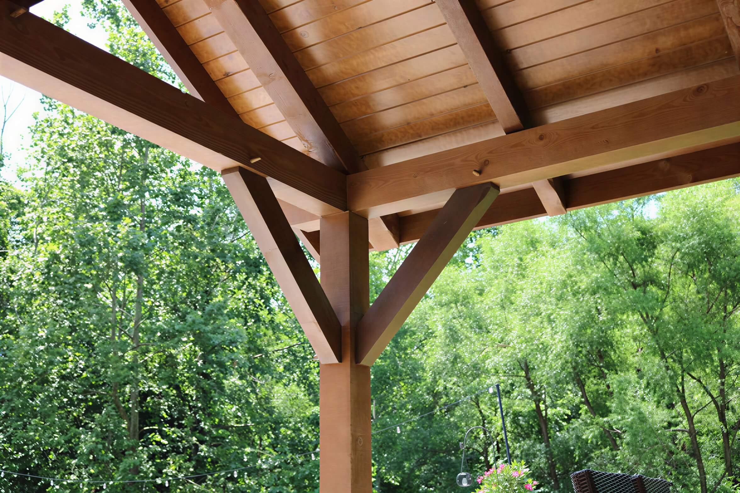 Close-up view of Brookside Timber Frame Forest Retreat Pavilion highlights its sturdy wooden beams and detailed craftsmanship against a leafy forest backdrop