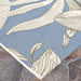 Close-up of Couristan Dolce Indoor/Outdoor Rug - Flora/Ice displays a smooth corner laying flat on a stone patio
