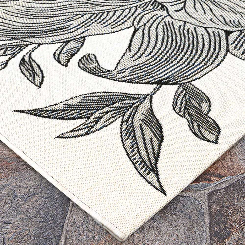 Close-up of Couristan Dolce Indoor/Outdoor Rug - Flora/Snow displays the detailed black floral lines against a textured snow-white surface on stone flooring