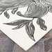 Close-up of Couristan Dolce Indoor/Outdoor Rug - Flora/Snow displays the detailed black floral lines against a textured snow-white surface on stone flooring