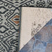 Close-up of Couristan Dolce Indoor/Outdoor Rug - Mala/Smoke shows its corner flipped over to reveal a woven beige backing against a stone floor