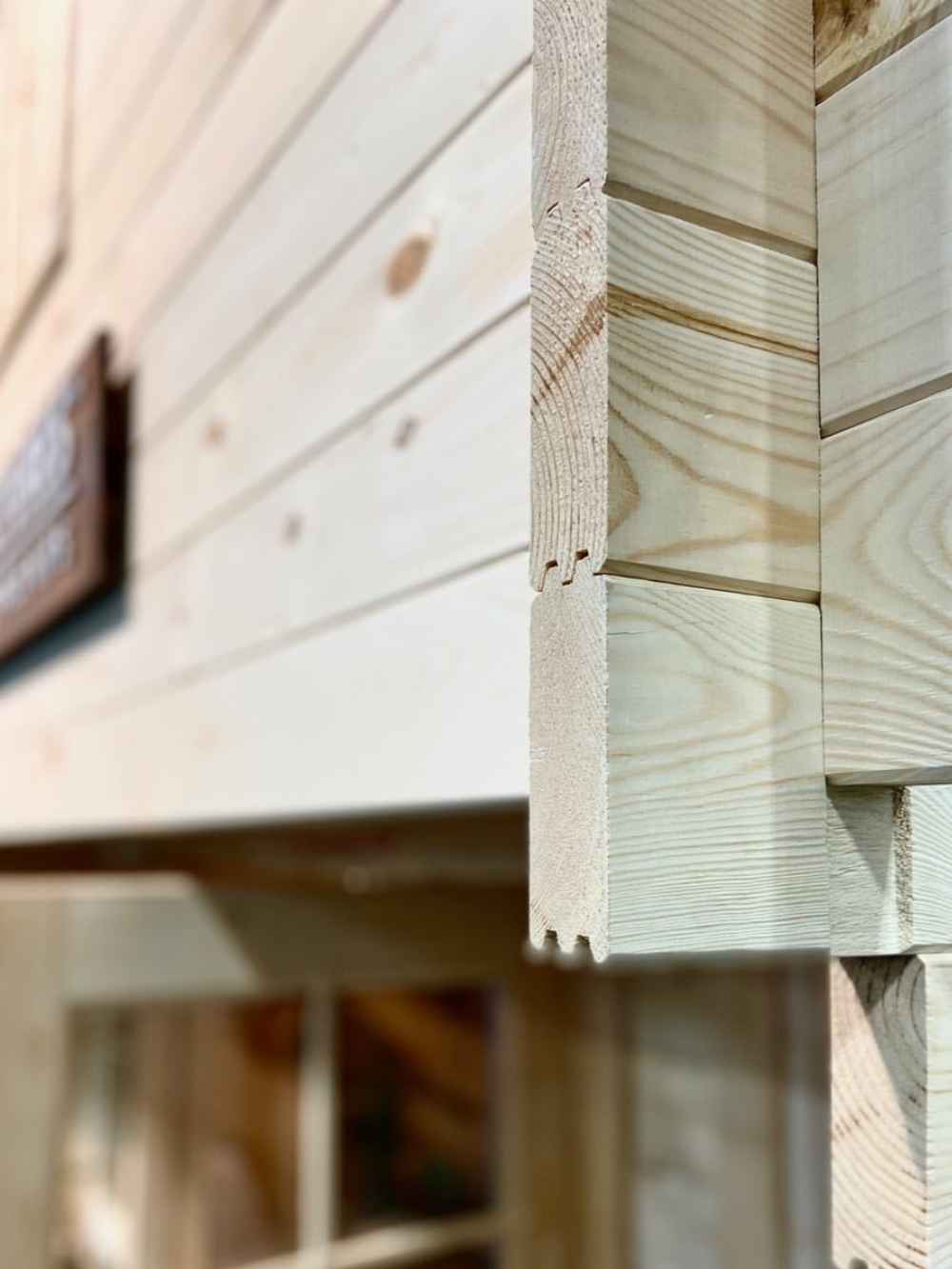 Close-up of the corner joint on the Sawmill Structures Grand Loft 107 Deluxe DD Garden Room reveals interlocking woodwork with smooth, unfinished timber panels