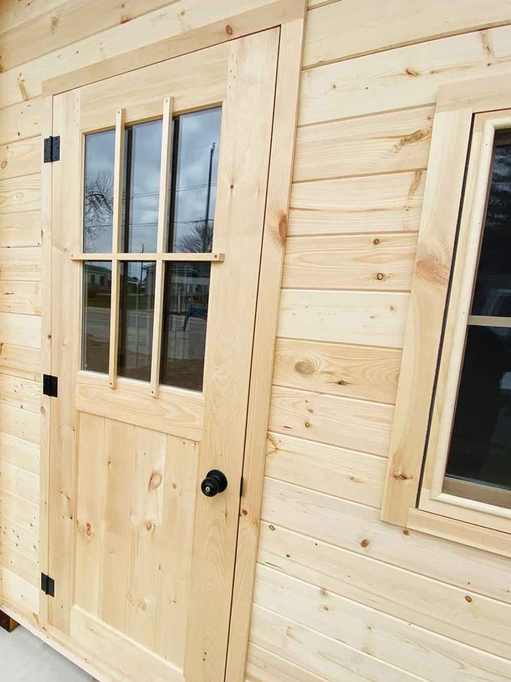 Close-up of the door and a nearby window on the Sawmill Structures Bluewater Den 67 Garden Room, highlighting the wood grain and sturdy black hardware