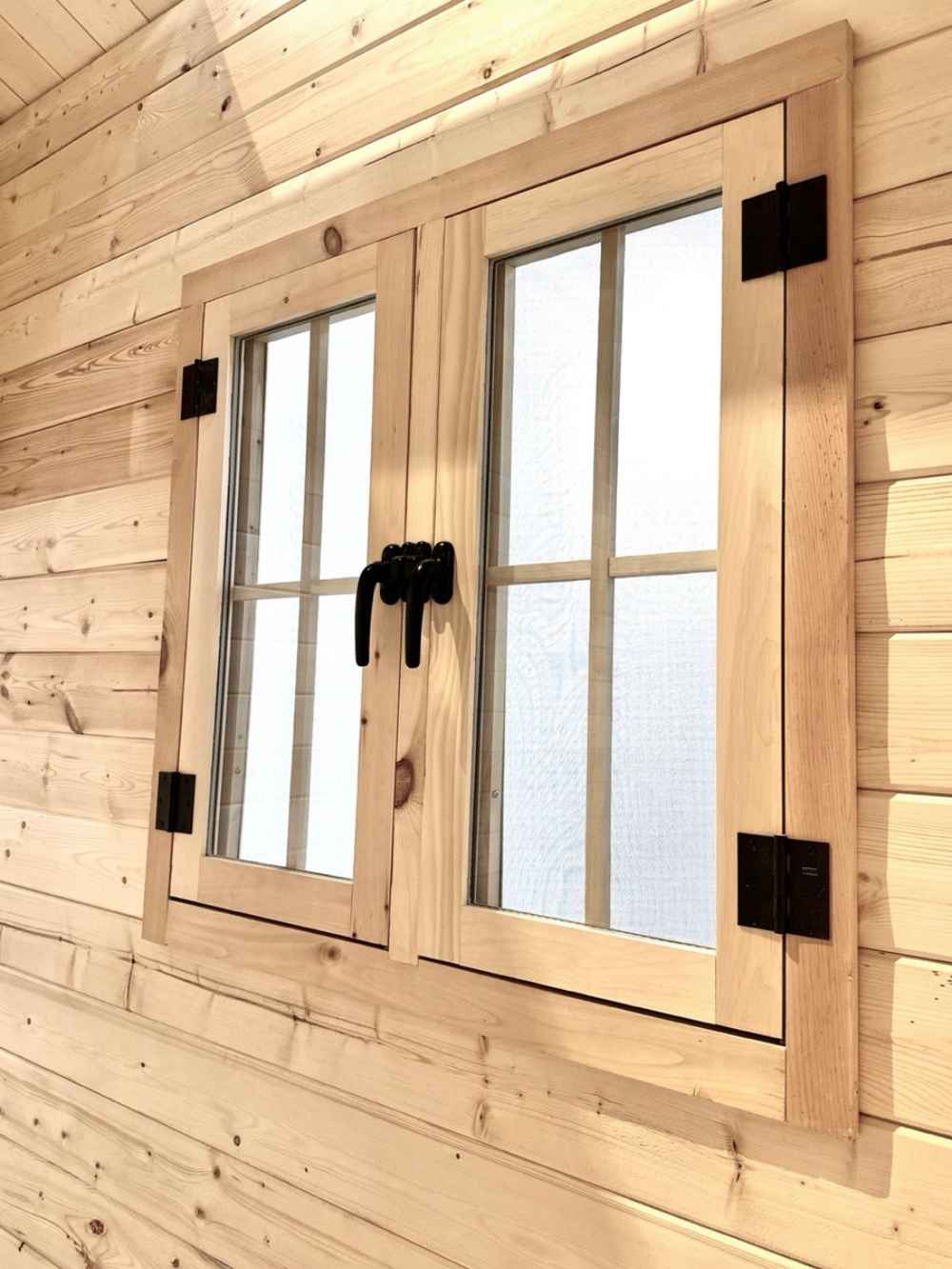 Close-up shows a sturdy double-pane wooden window with black hardware inside the Sawmill Structures Multi Cube Versa 100 Garden Room