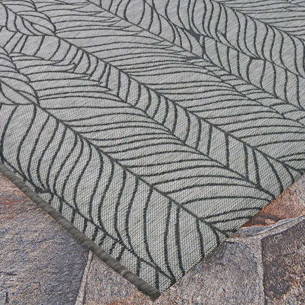 Close-up view of Couristan Dolce Indoor/Outdoor Rug - Majorelle/Silver-Black shows the black leaf pattern on a silver background lying flat on a stone patio
