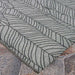 Close-up view of Couristan Dolce Indoor/Outdoor Rug - Majorelle/Silver-Black shows the black leaf pattern on a silver background lying flat on a stone patio