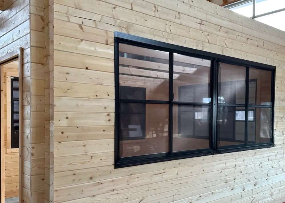 Close-up view of a large black-trimmed window set in a light wood-paneled wall inside Sawmill Structures Eze Breeze Sunroom Cabin