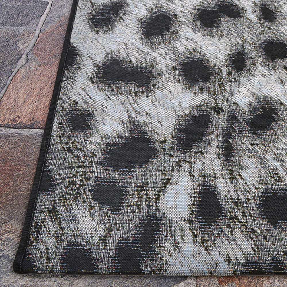 Closer view of Couristan Dolce Indoor/Outdoor Rug - Lynx/Ivory-Charcoal displays the corner lying flat on a stone patio