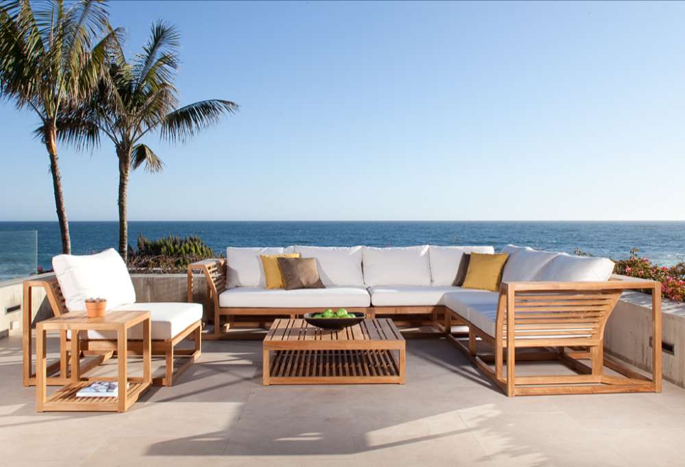 Coastal patio scene features a large outdoor sectional set that includes Westminster Teak Maya Slipper Chair, overlooking the ocean with palm trees nearby