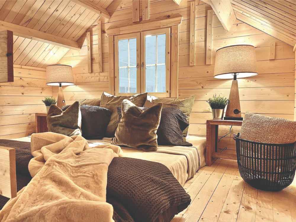 Comfy lounge nook with plush pillows, soft lighting, and a central window is featured in the Sawmill Structures Ontario Grand Loft 107 SD Garden Room