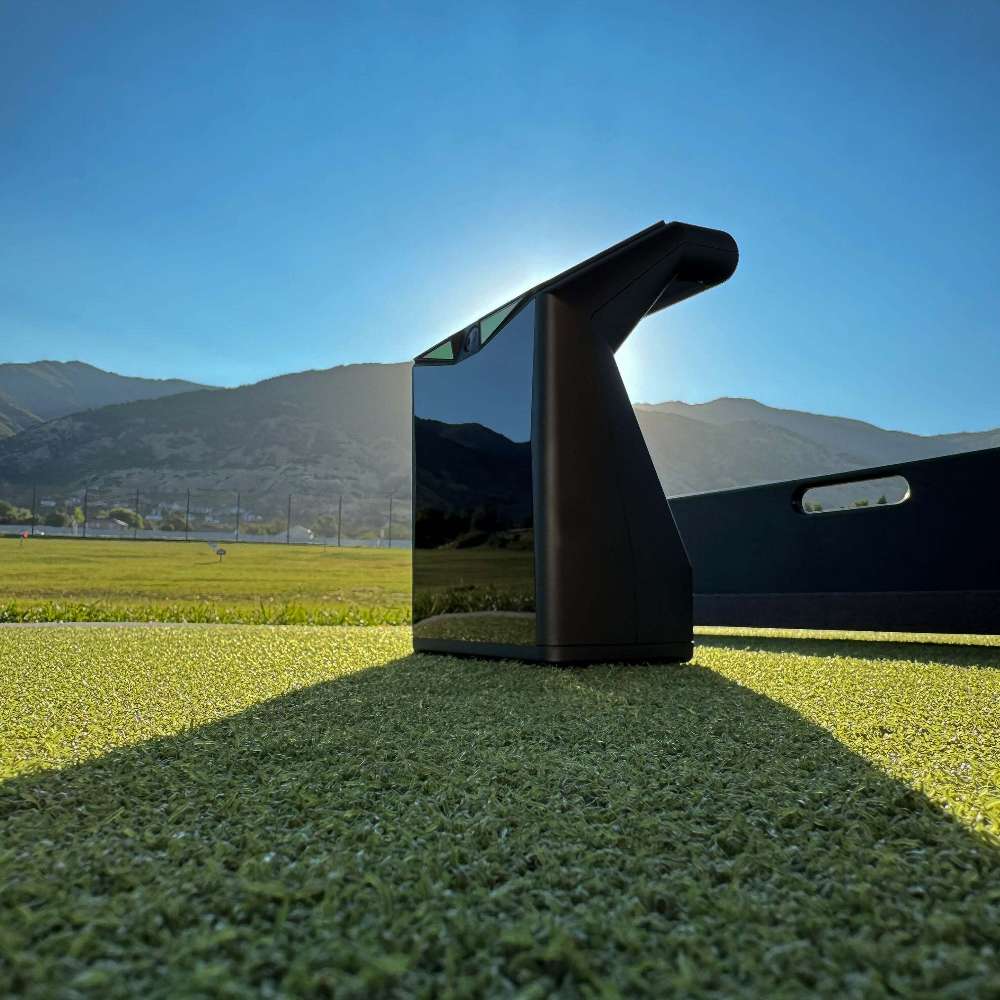 Compact black device sitting on green turf at a range with TruGolf LaunchBox Golf Launch Monitor w/ E6 CONNECT Home + Premium centered in the scene