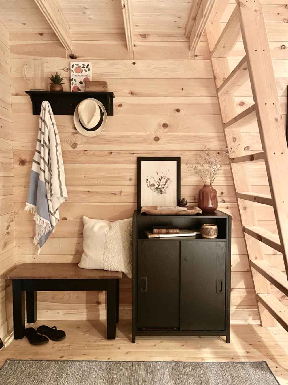 Compact entryway in the Sawmill Structures Ontario Grand Loft 107 SD Garden Room includes a black bench, wall hooks, and wood-paneled walls