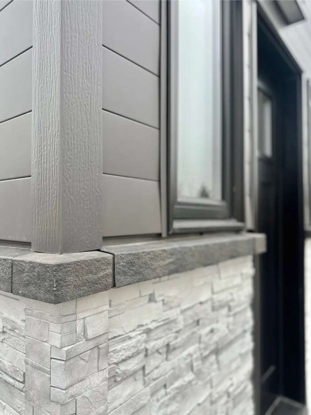 Corner exterior of Sawmill Structures Wanderlove Tiny Home shows detailed faux-stone siding beneath sleek black-trimmed windows