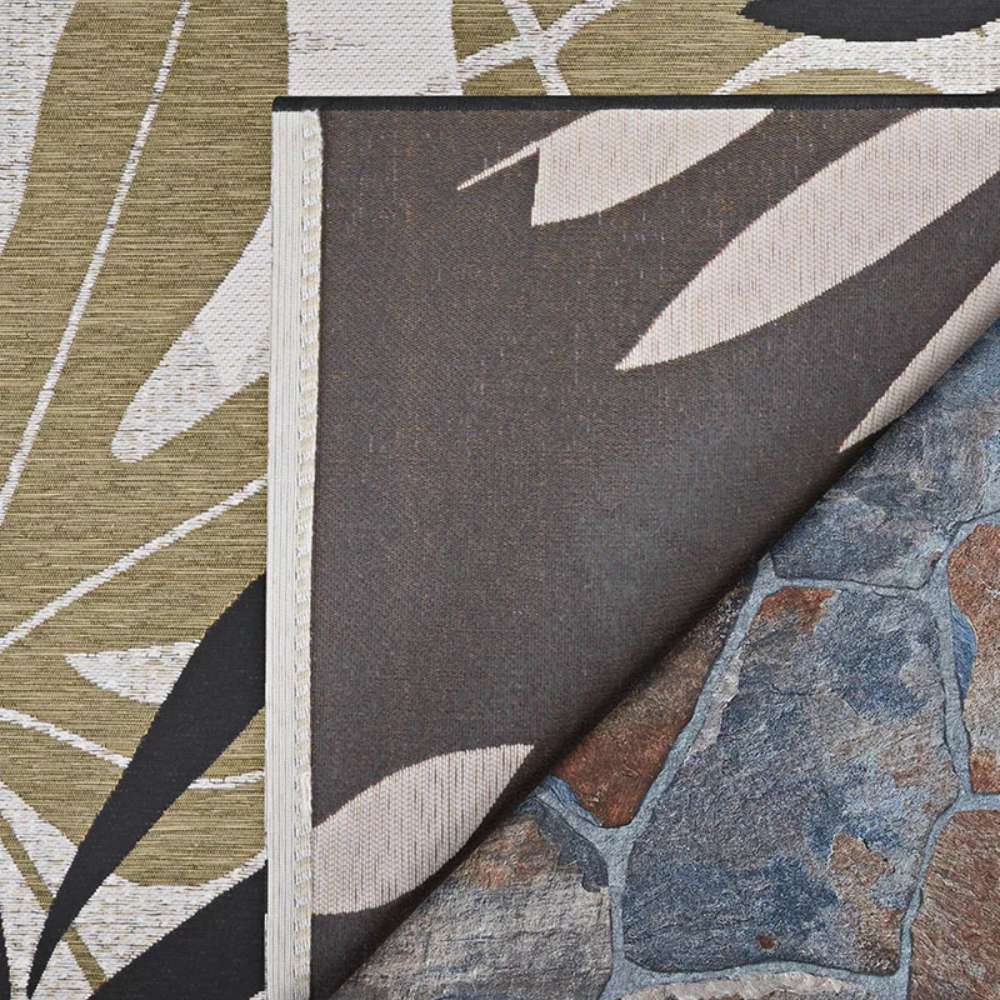 Corner of Couristan Dolce Indoor/Outdoor Rug - Aralia/Naturals-Cool Onyx flipped over, revealing its stitched edge and backing on a stone patio