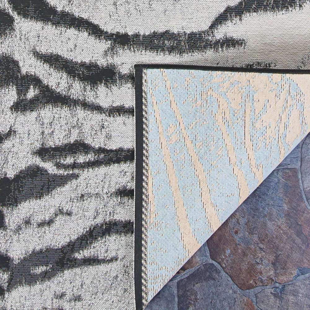 Corner of Couristan Dolce Indoor/Outdoor Rug - Bengal/Ivory flipped over showing the tightly woven backing and front tiger-stripe pattern