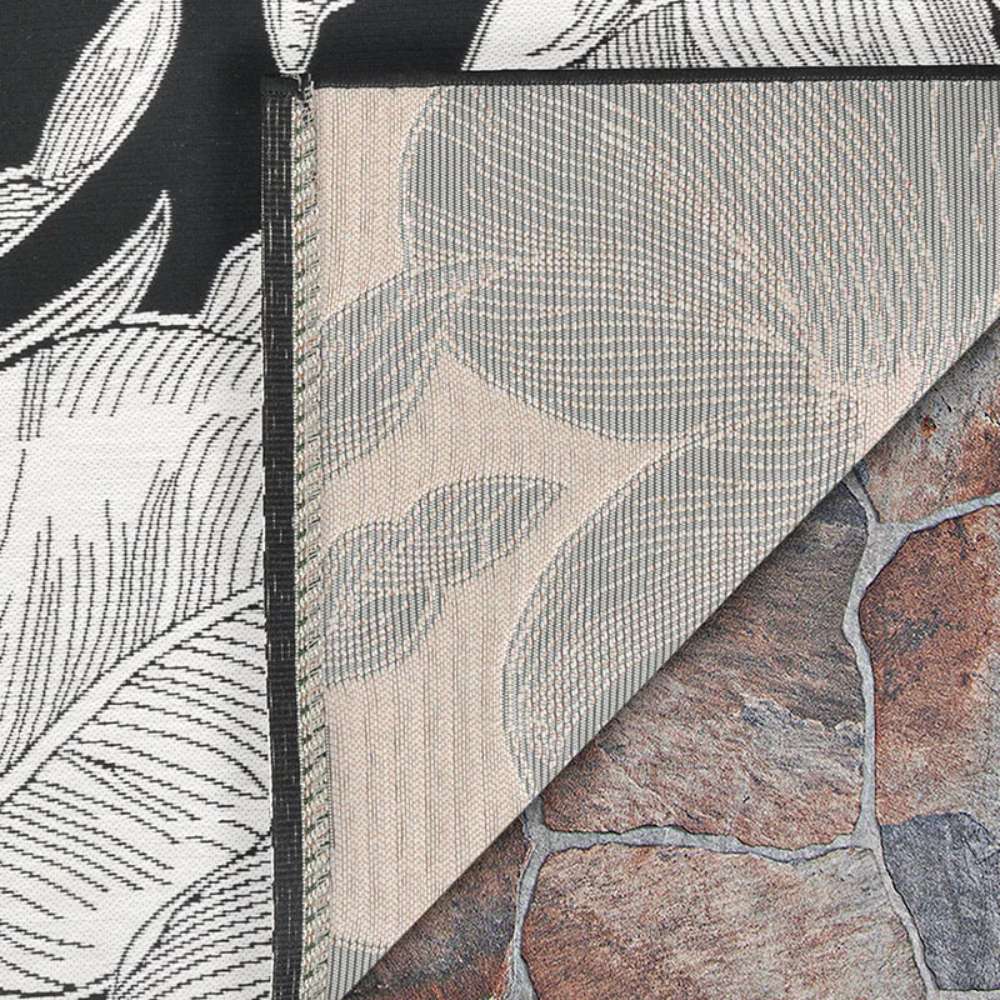 Corner of Couristan Dolce Indoor/Outdoor Rug - Flora/Nero shows the black and cream floral design on top and a glimpse of the underside weave