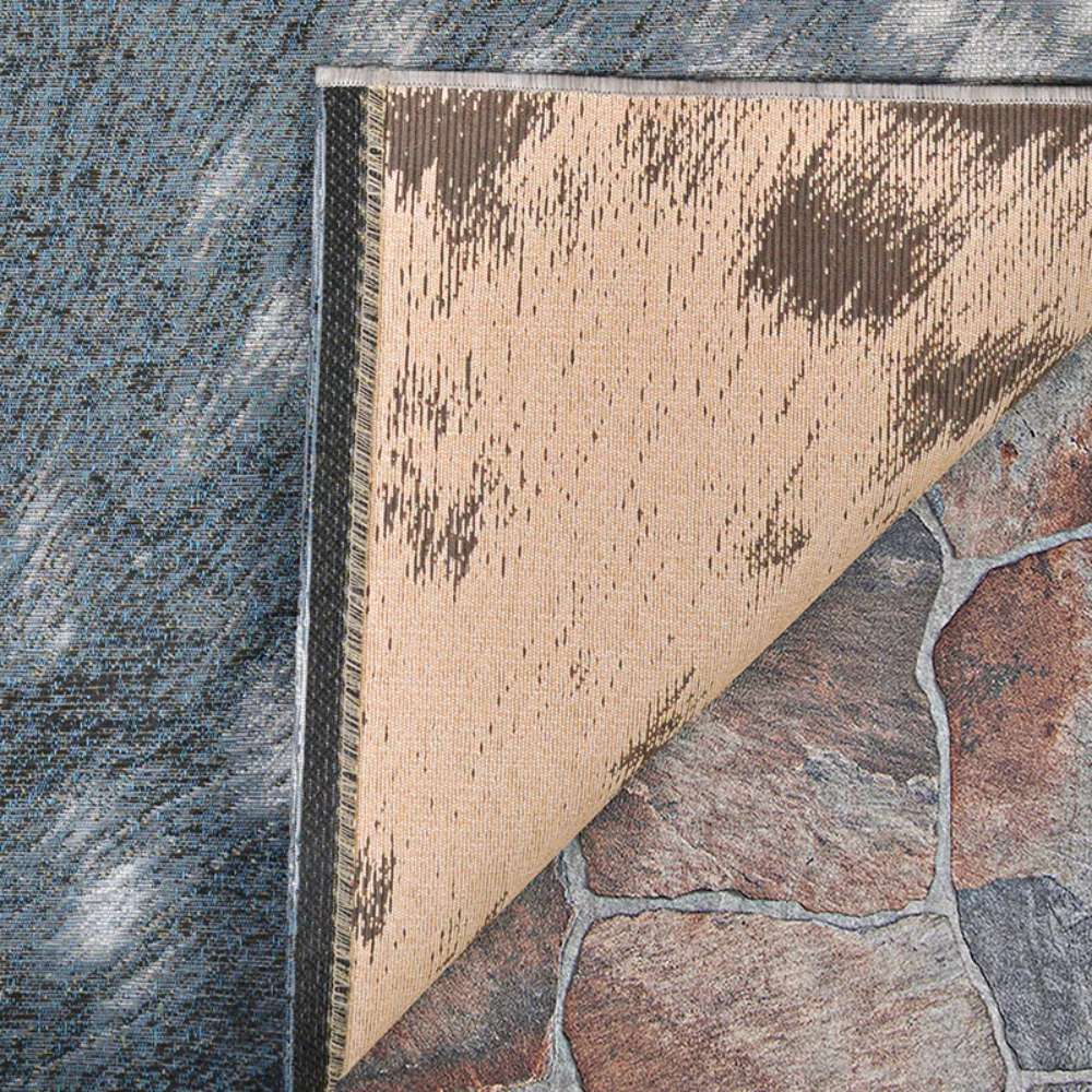 Corner of Couristan Dolce Indoor/Outdoor Rug - Hyena/Denim-Silver is flipped over showing its underside and texture detail