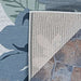 Corner of Couristan Dolce Indoor/Outdoor Rug - Novella/Grey folded back, revealing its tightly woven underside over a stone patio