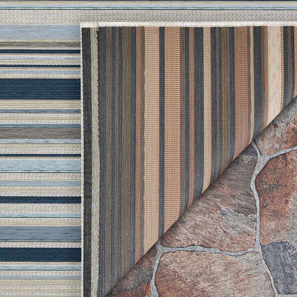 Corner of Couristan Dolce Indoor/Outdoor Rug - Striped/Nautical is flipped to show its reversible design over stone flooring