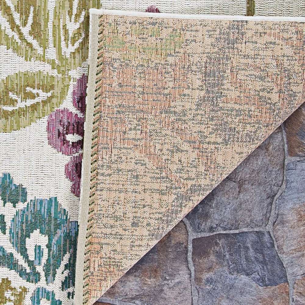 Corner of Couristan Dolce Indoor/Outdoor Rug - Tivoli/Ivory-Multi flipped to reveal its tightly woven underside on a stone patio
