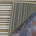 Corner of the Couristan Cape Indoor/Outdoor Rug - Brockton/Light Brown-Ivory flipped up, revealing the striped backing and underside