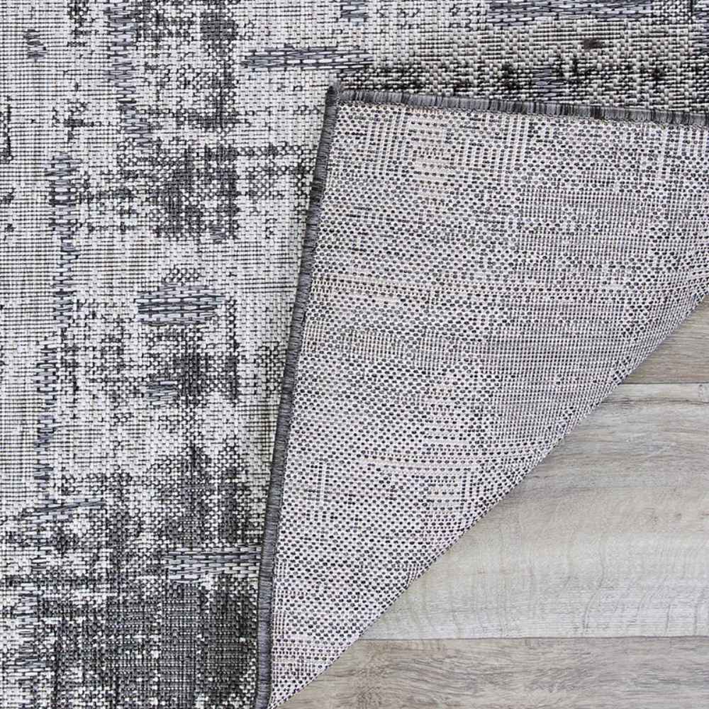 Corner of the Couristan Charm Indoor/Outdoor Rug - Tiverton/Anthracite-Light Grey is flipped to show its underside and weave construction
