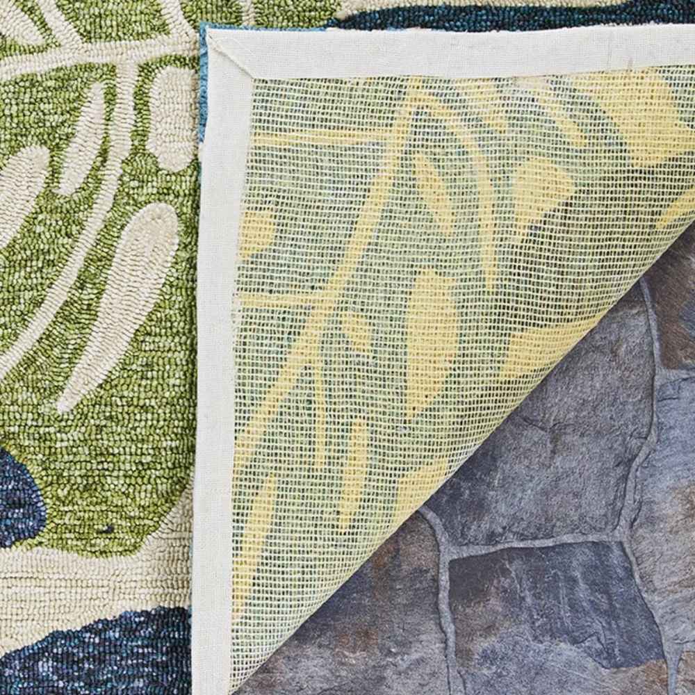 Corner of the Couristan Covington Indoor/Outdoor Rug - Monstera/Cream-Multi is flipped to reveal a mesh backing over a stone surface