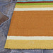 Corner of the Couristan Covington Indoor/Outdoor Rug - Sherbet Stripe/Multi shows its sturdy weave and warm orange and yellow stripes on stone flooring