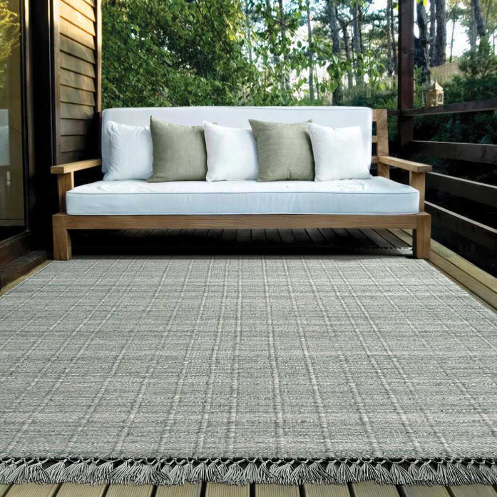 Couristan Ascot Indoor/Outdoor Rug - Windowpane/Celedon is laid out on a patio beneath a wooden sofa, creating a calm, cozy outdoor space