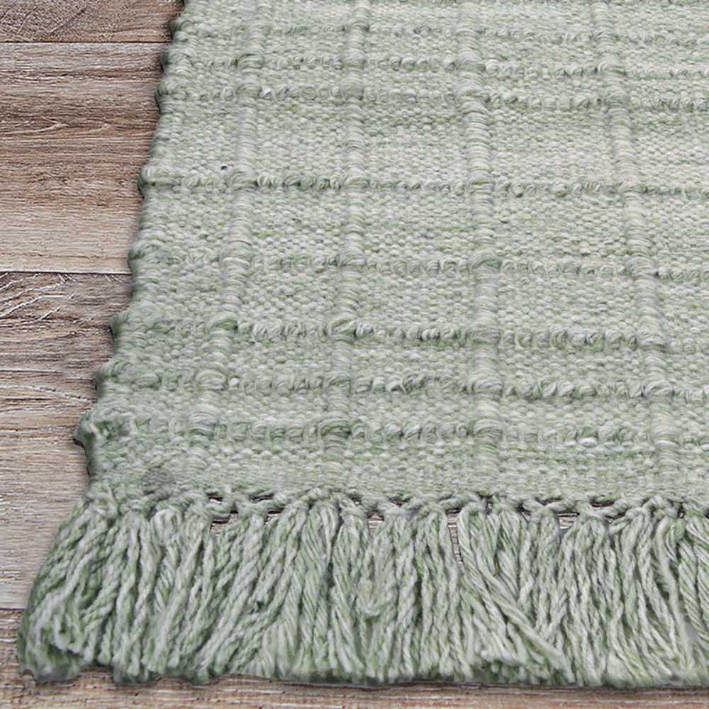 Couristan Ascot Indoor/Outdoor Rug - Windowpane/Celedon sits on a wood floor with detailed fringe and visible grid-like stitching