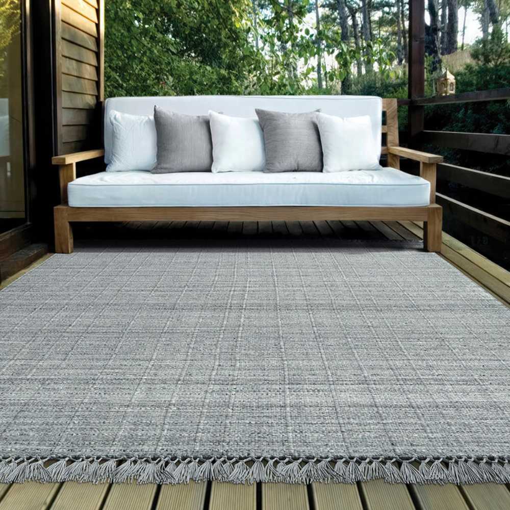 Couristan Ascot Indoor/Outdoor Rug - Windowpane/Tweed is displayed on a wooden deck beneath a modern outdoor sofa, blending seamlessly with the natural setting
