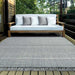 Couristan Ascot Indoor/Outdoor Rug - Windowpane/Tweed is displayed on a wooden deck beneath a modern outdoor sofa, blending seamlessly with the natural setting
