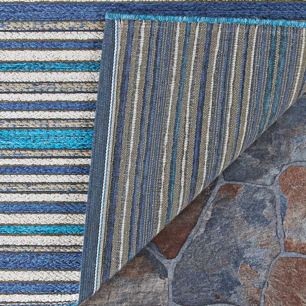 Couristan Cape Indoor/Outdoor Rug - Brockton/Cobalt-Teal is partially flipped to show both its top pattern and the woven underside on a rustic tile floor