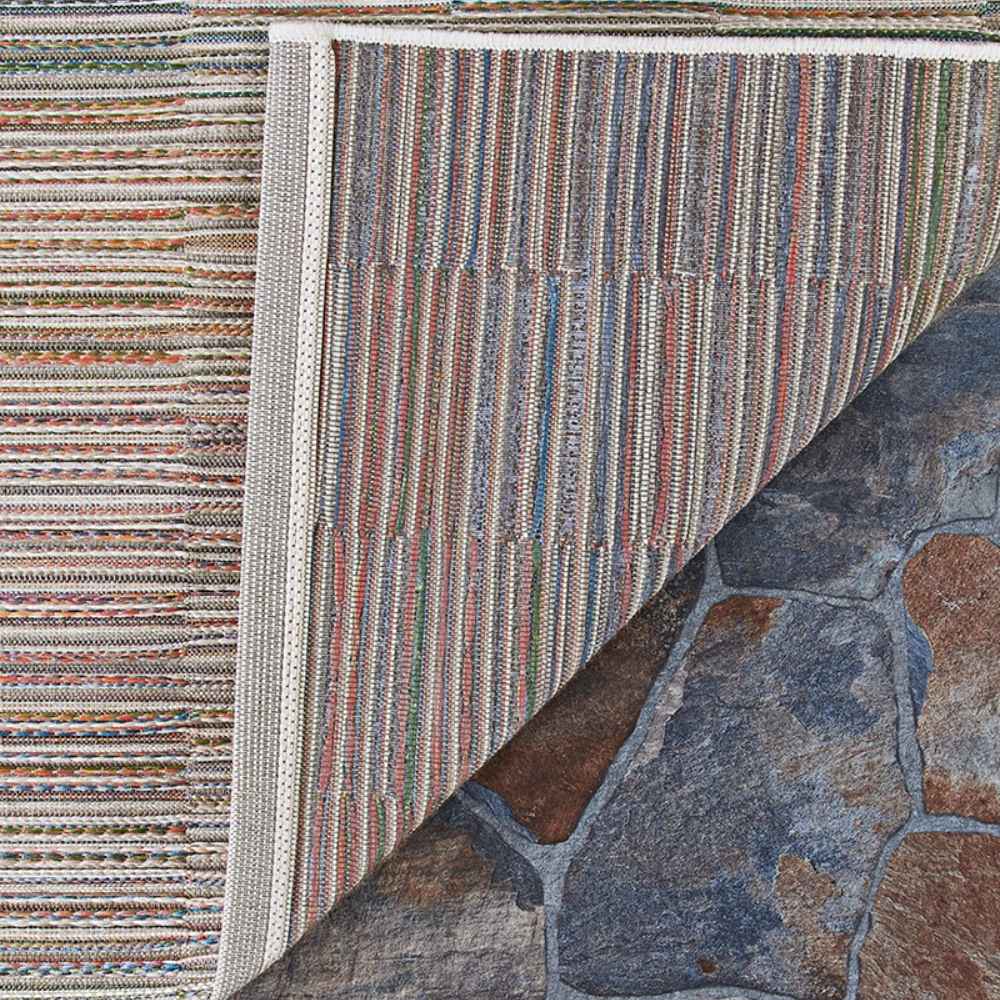 Couristan Cape Indoor/Outdoor Rug - Fayston/Multi is shown with a corner flipped to reveal its durable backing and colorful woven texture on stone flooring
