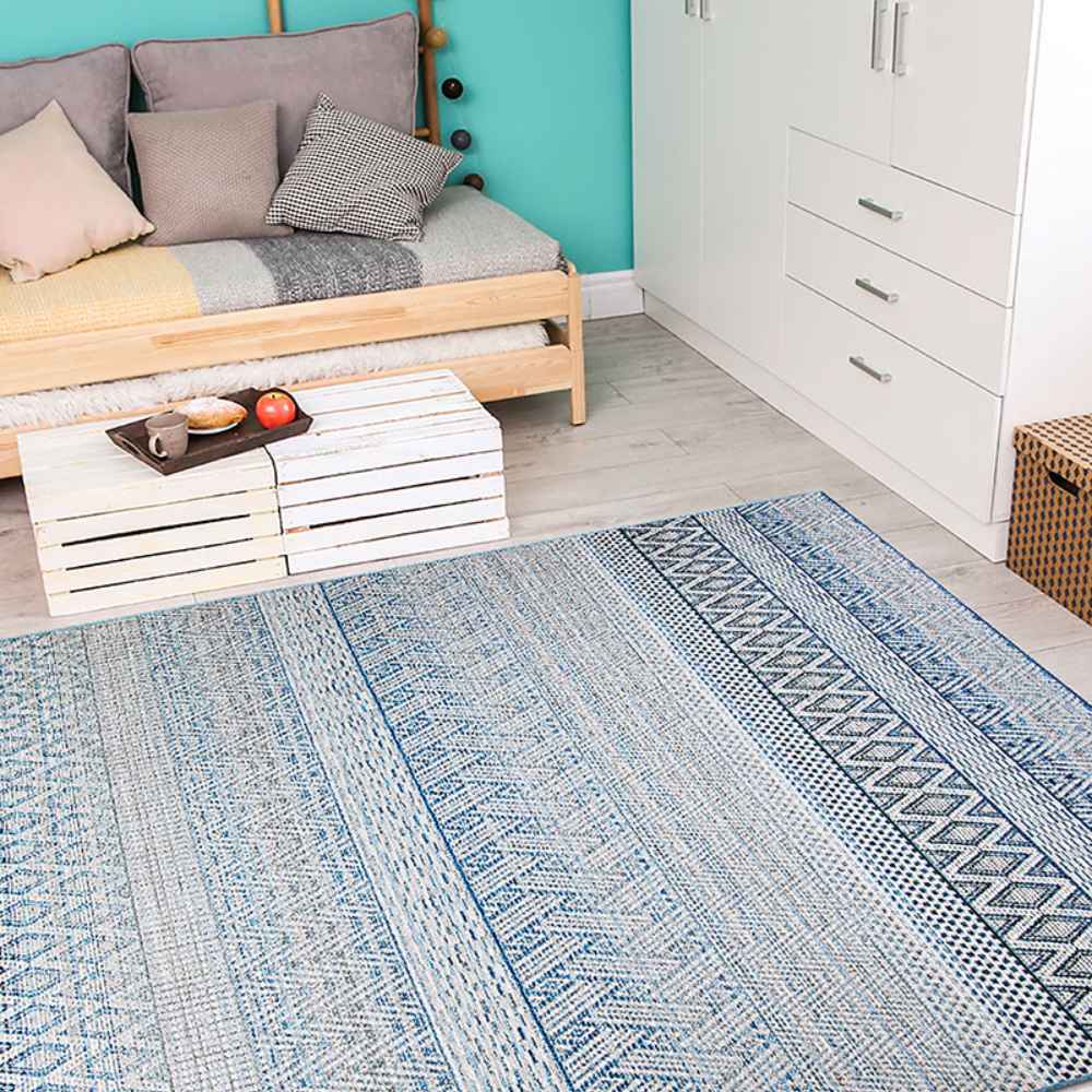 Couristan Cape Indoor/Outdoor Rug - Gables/Surf is laid out in a bright, modern room with a wooden daybed, white furniture, and turquoise walls