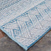 Couristan Cape Indoor/Outdoor Rug - Gables/Surf is partially rolled back on a stone surface to show off its tidy stitching and pattern consistency