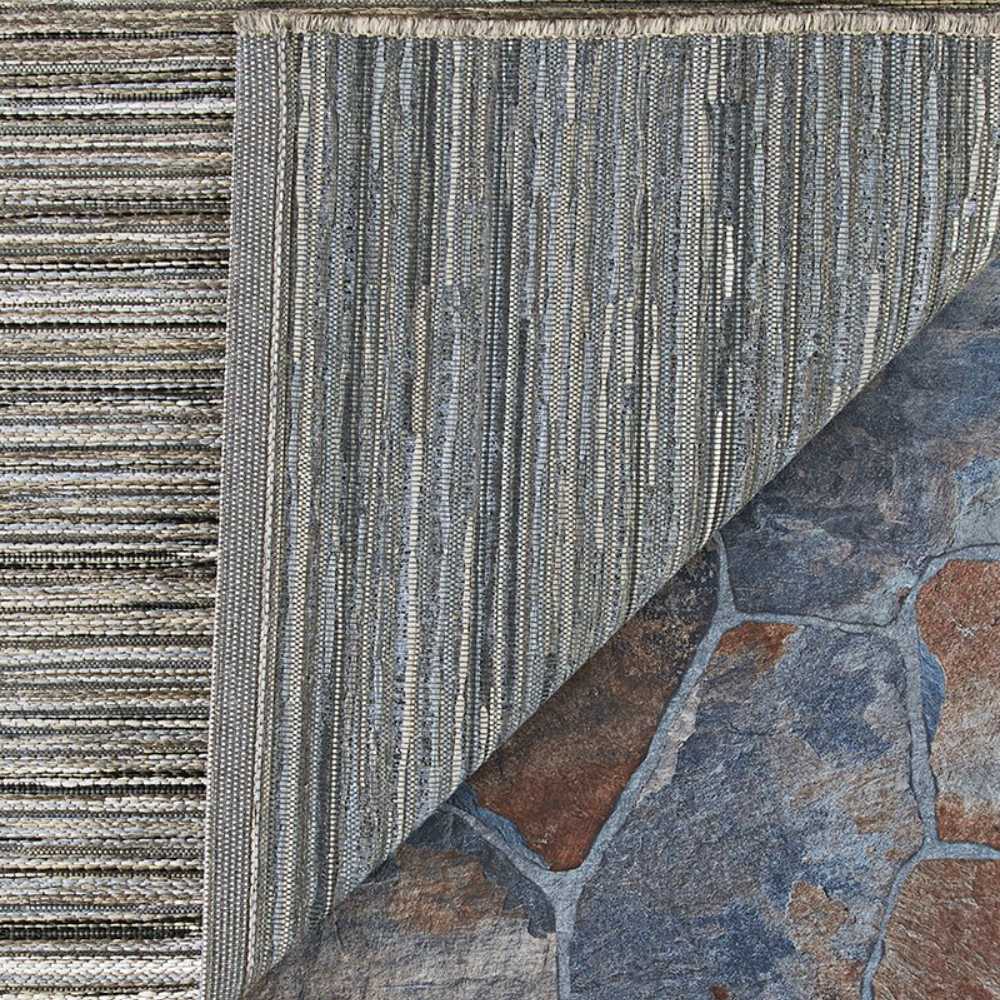 Couristan Cape Indoor/Outdoor Rug - Hinsdale/Light Brown-Silver is shown partially lifted to reveal its underside and the stone surface beneath it