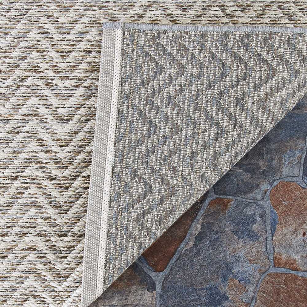 Couristan Cape Indoor/Outdoor Rug - Marion/Light Brown-Ivory is flipped at the corner, revealing its durable underside on a stone patio