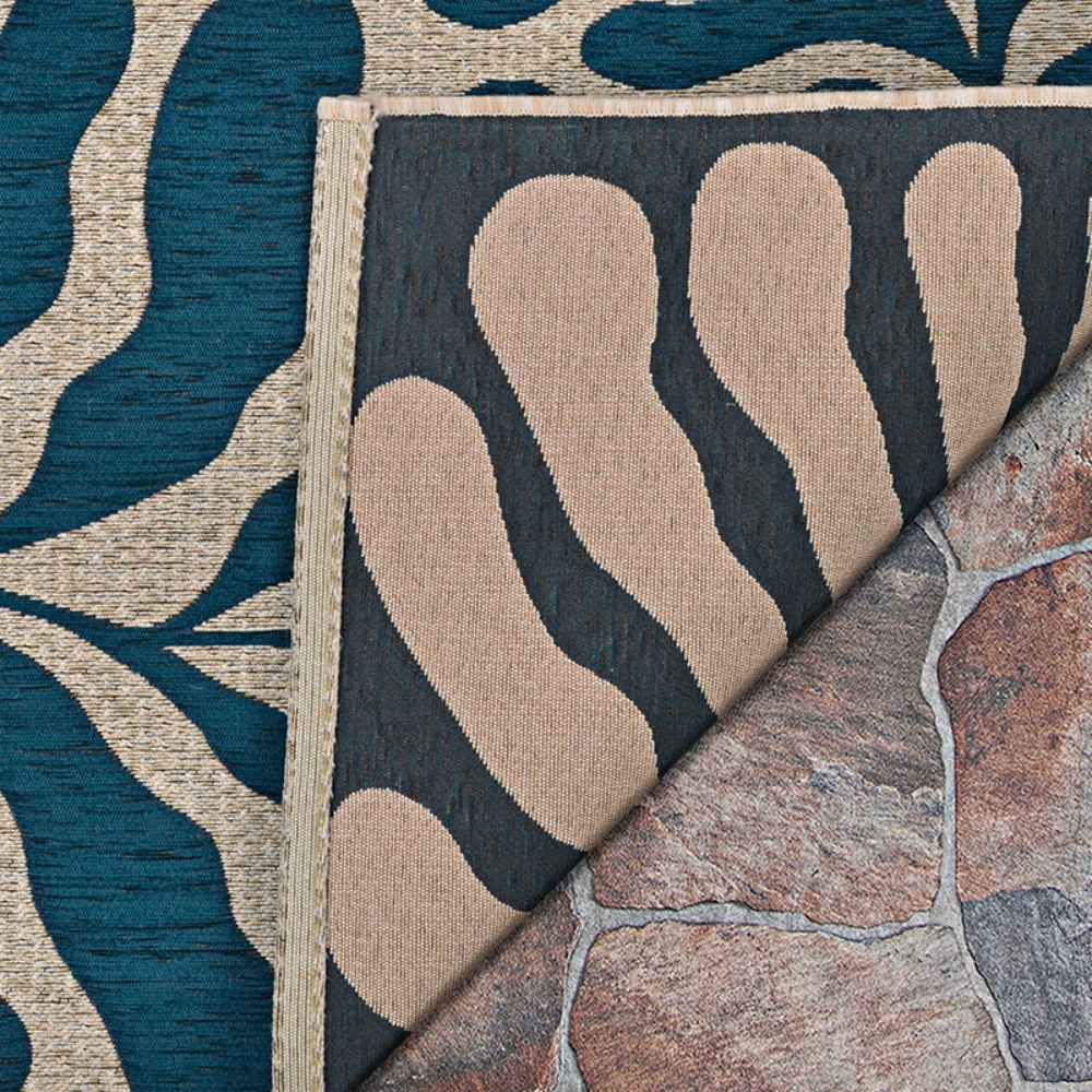 Couristan Castille Indoor/Outdoor Rug - Fiore/Petrol is flipped to show its backing and thick edges, laid over a textured stone floor