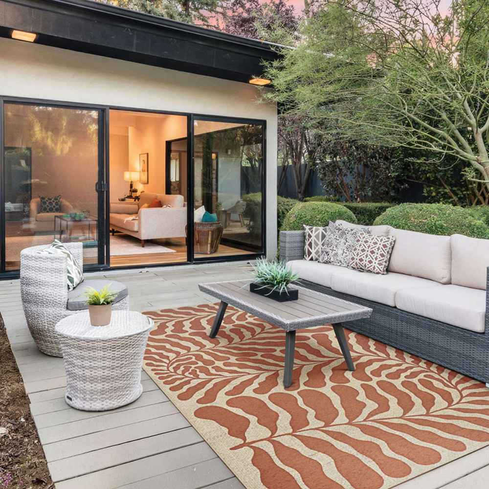 Couristan Castille Indoor/Outdoor Rug - Fiore/Terra-Cotta is laid out on a stylish patio under outdoor furniture