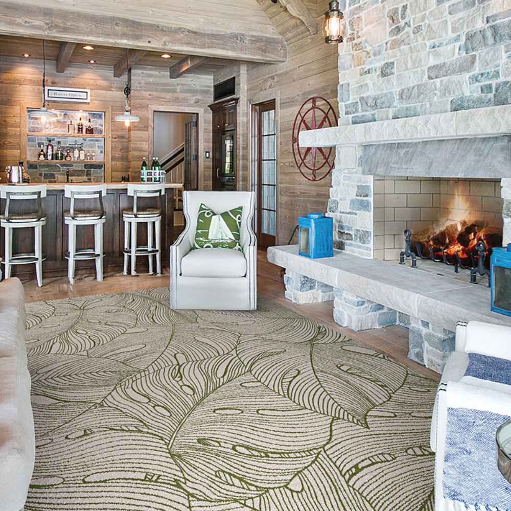 Couristan Castille Indoor/Outdoor Rug - Palma/Rouge lies in a cozy living room with a fireplace, bar, and wood-paneled walls