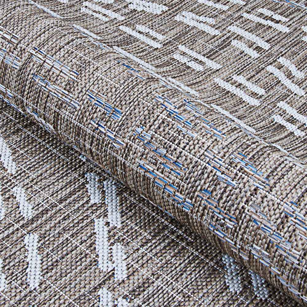 Couristan Charm Indoor/Outdoor Rug - Aurora/Twig is partially rolled to highlight its thick weave and subtle mix of twig, ivory, and blue tones