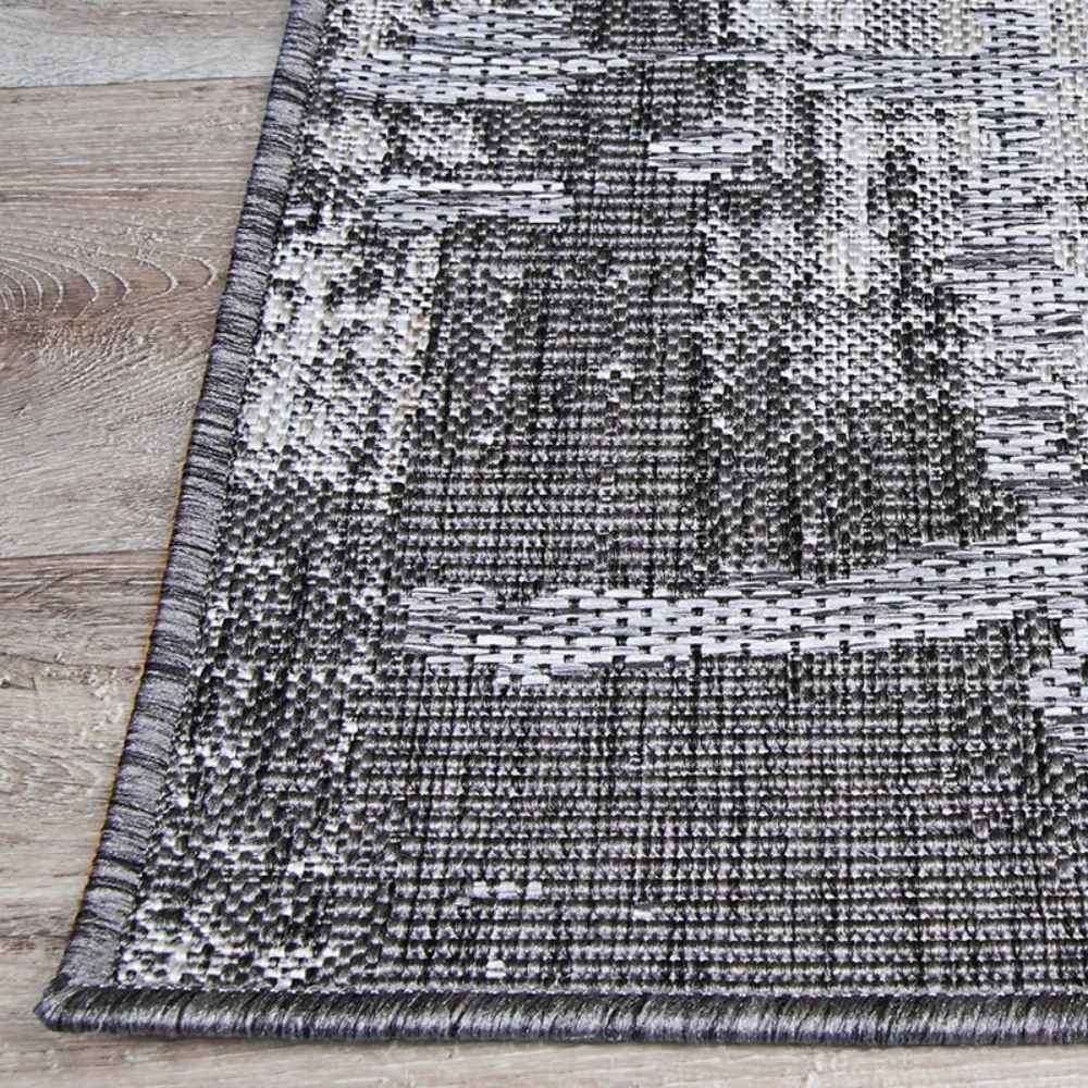 Couristan Charm Indoor/Outdoor Rug - Tiverton/Anthracite-Light Grey is shown with neat, stitched edges on a light wood floor