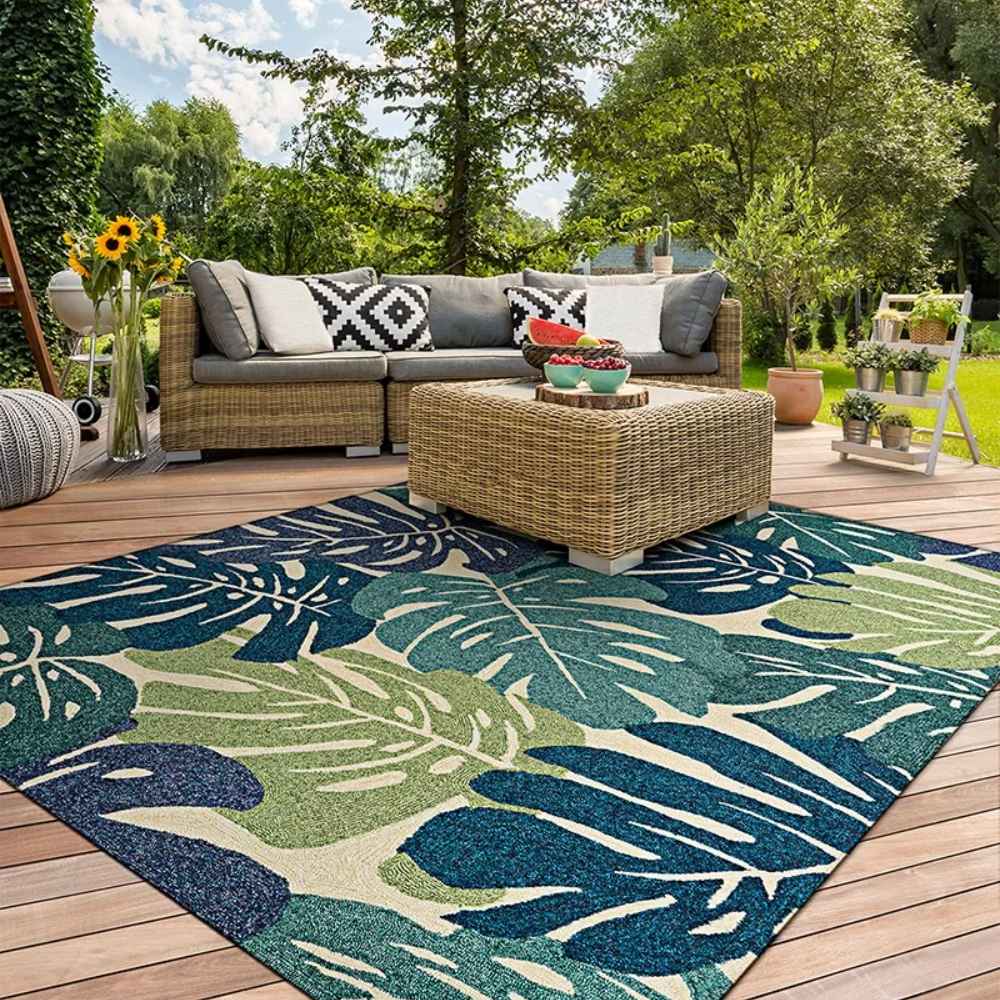 Couristan Covington Indoor/Outdoor Rug - Monstera/Cream-Multi adds a tropical touch to a cozy outdoor patio setup with wicker furniture