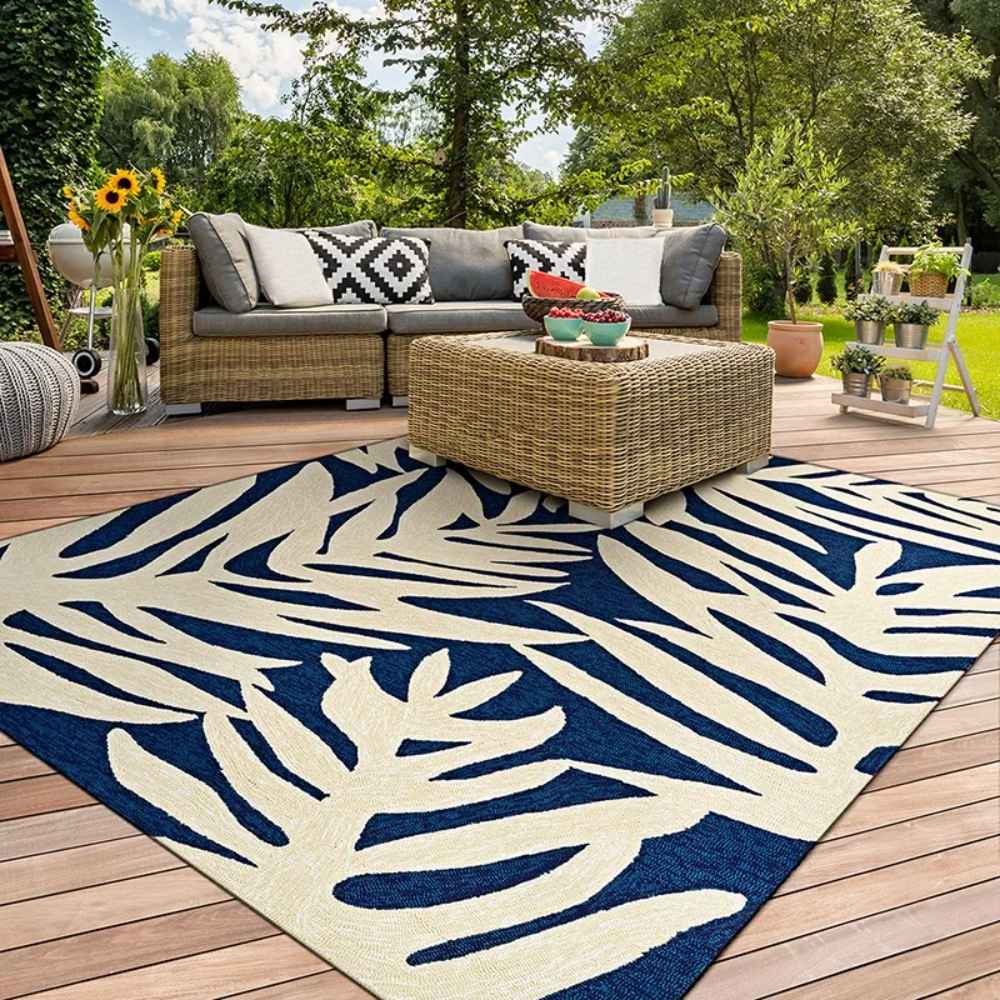 Couristan Covington Indoor/Outdoor Rug - Palms/Navy adds a vibrant touch under a wicker coffee table on a sunny outdoor patio