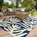 Couristan Covington Indoor/Outdoor Rug - Palms/Navy adds a vibrant touch under a wicker coffee table on a sunny outdoor patio