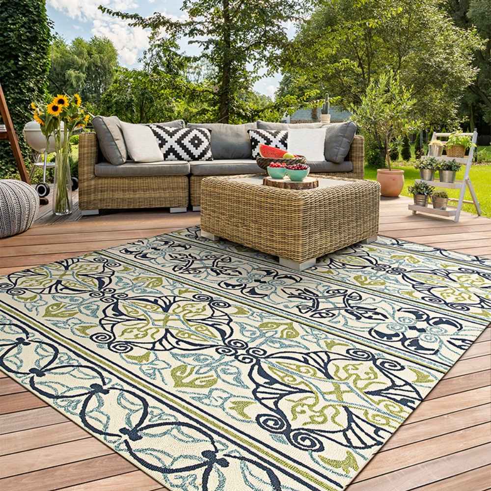 Couristan Covington Indoor/Outdoor Rug - Pegasus/Ivory-Navy-Lime is displayed on a sunny deck with wicker furniture and vibrant greenery