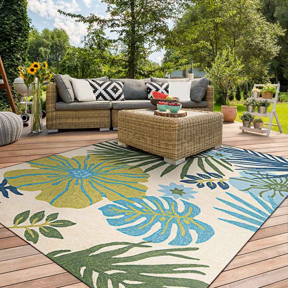Couristan Covington Indoor/Outdoor Rug - Summer Laelia/Ivory-Fern lies under a patio set, adding a splash of tropical flair to a sunlit wooden deck